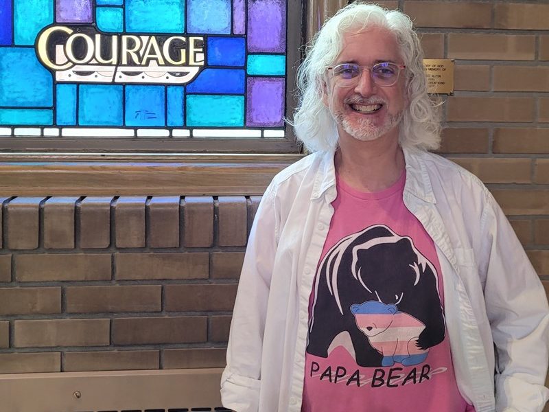 author wearing a pink shirt described in the post, standing beside a window with the word "courage"