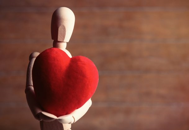 wooden mannequin holding a red heart-shaped pillow