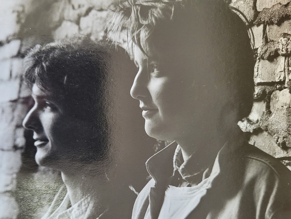 b&w of young man's and woman's heads with a brick wall in the background