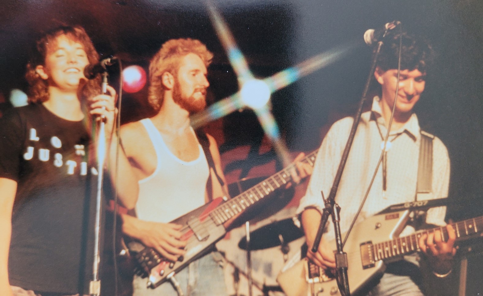 3 musicians on a stage: a female singer, a male bass player, and a male guitar player, all in their early 20s